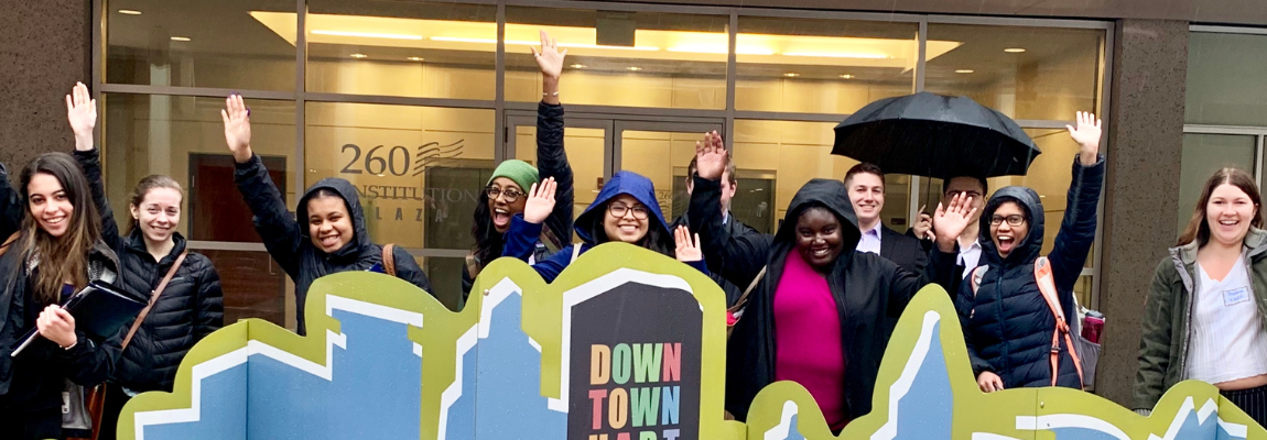 Students waving in front of Downtown sign